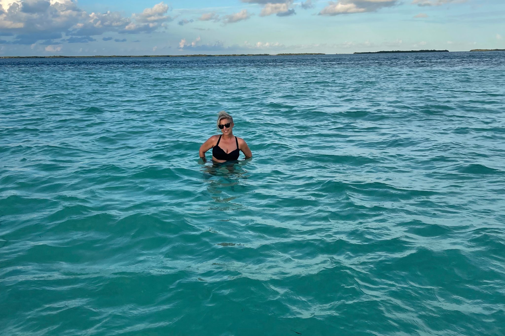 Mandy standing on a sandbar in the middle of the clear blue waters of Key West, looking at the camera with a confident expression, showcasing her love for traveling and living life to the fullest