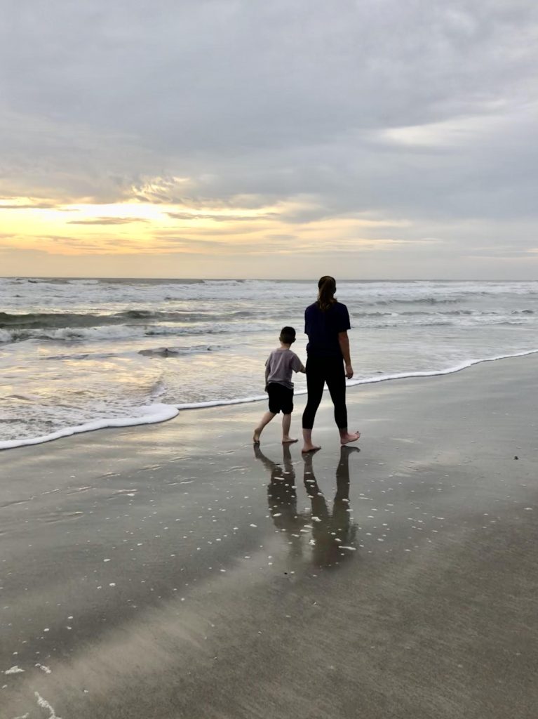 A serene sunset at the beach with a parent and child walking along the shoreline