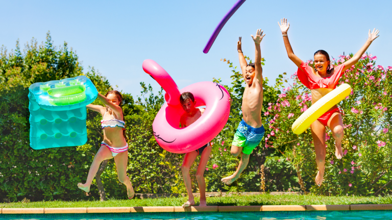 Four kids jumping into a swimming pool with colorful floats, splashing and laughing together during a fun summer day.
