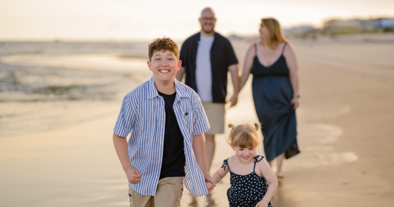 Lauren and her husband stand in the background watching as their two children run ahead on a sandy beach, capturing the bittersweet beauty of parenting in different stages.