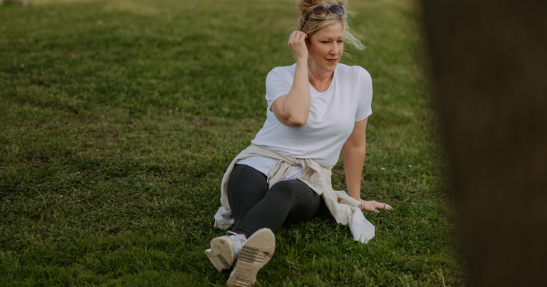 A calm woman sitting in the grass, taking a quiet moment to reset her mind and breathe outdoors.
