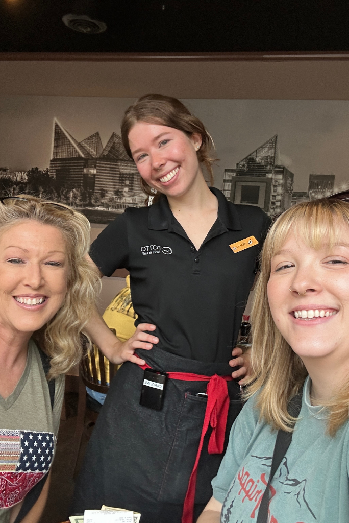 Mandy and Lauren from The Empty Nest Mom smiling with their friendly waitress during a casual lunch outing