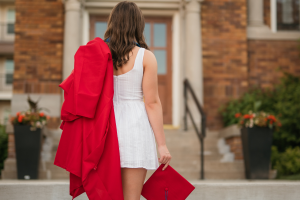 Mother walking toward graduation holding red cap and gown symbolizing raising independent daughters and letting go
