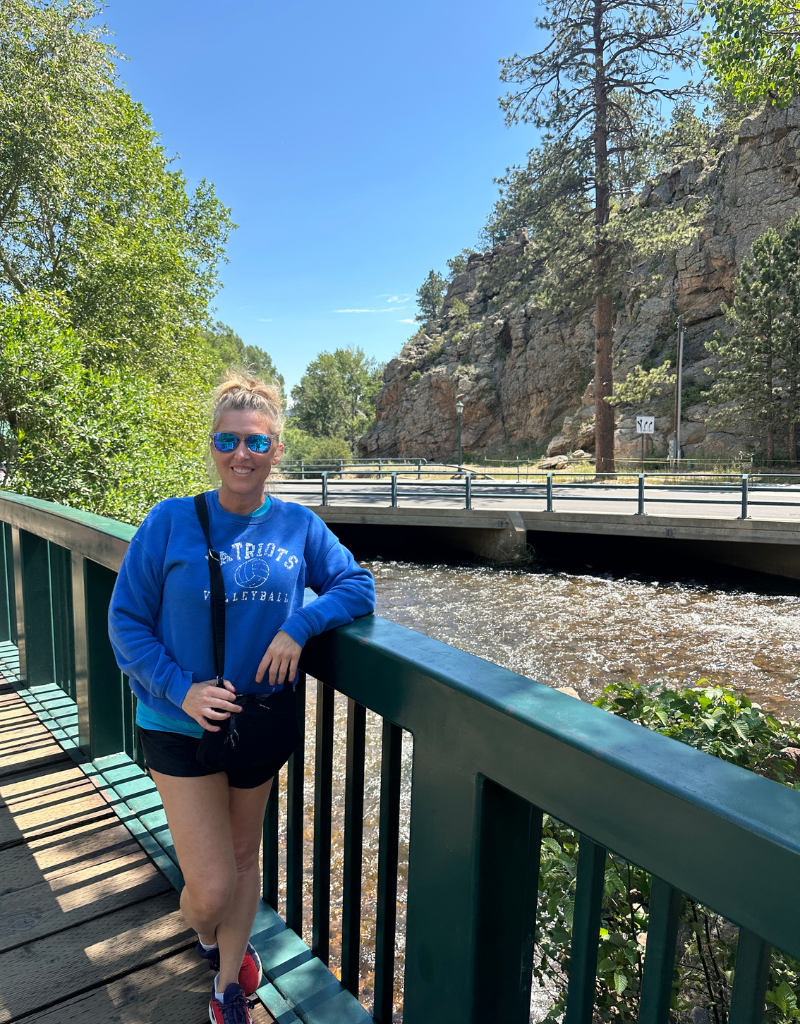 woman standing on bridge in Estes Park Colorado during mother daughter girls trip with mountain and river views