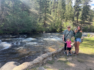 mother daughter girls trip in Estes Park Colorado with granddaughter and dog standing by river in mountains
