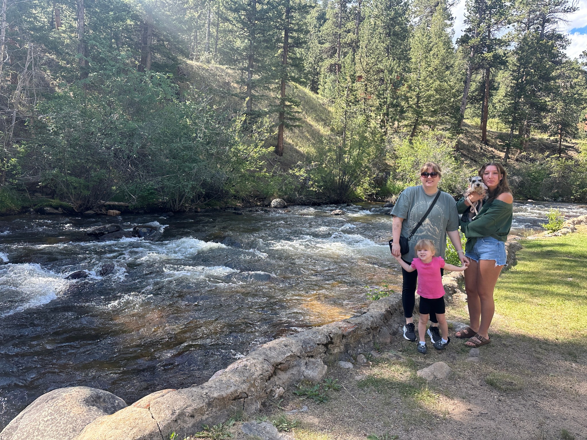 mother daughter girls trip in Estes Park Colorado with granddaughter and dog standing by river in mountains