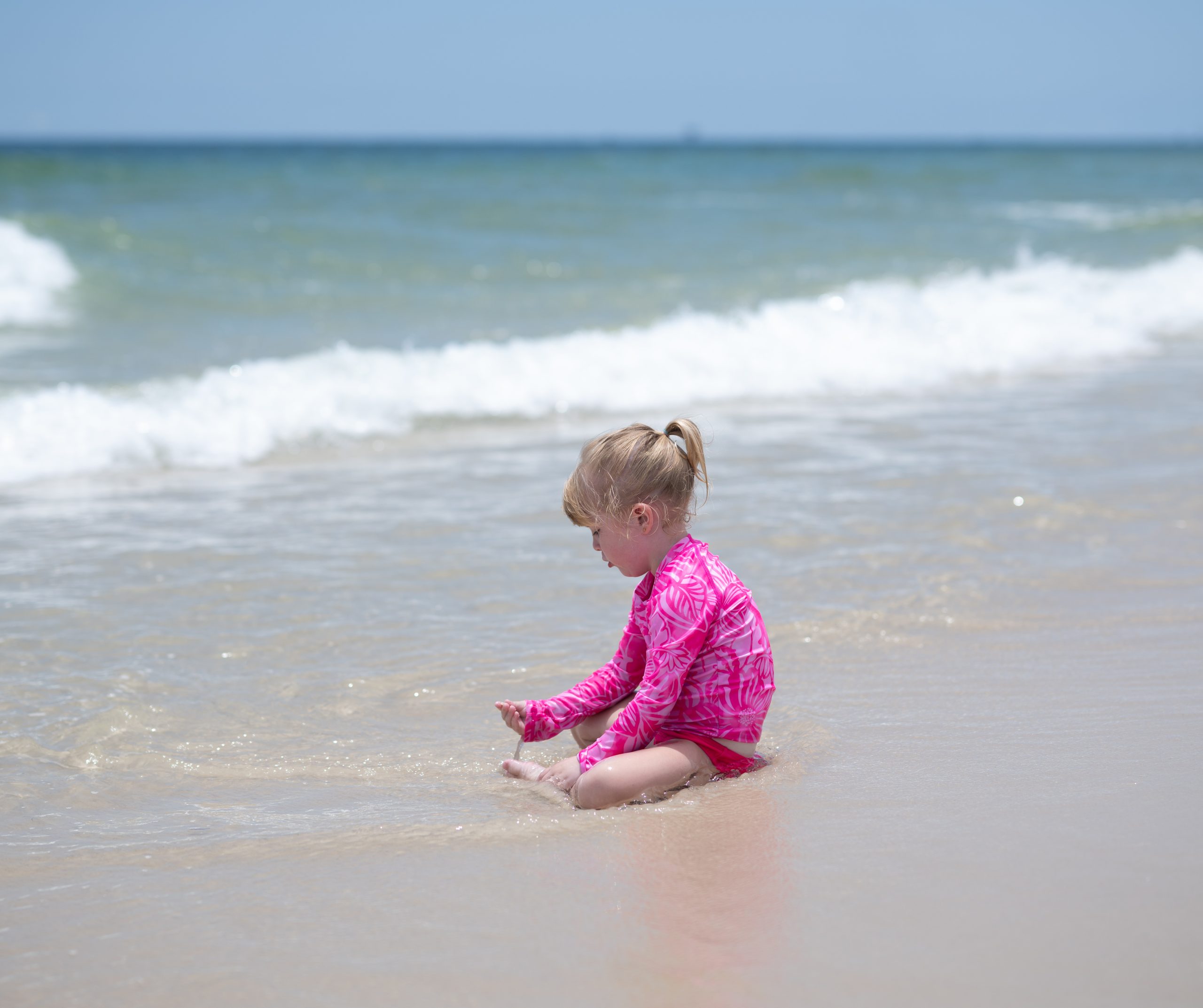 Quinn in a bright pink swimsuit playing at Gulf Shores Alabama beach