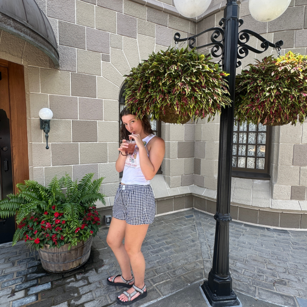 Gracie standing by hanging baskets of flowers at Epcot drinking a drink