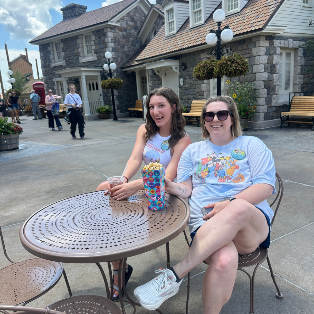 Gracie and Lauren sitting at the table at disney enjoying her first drink and popcorn in Canada at Epcot