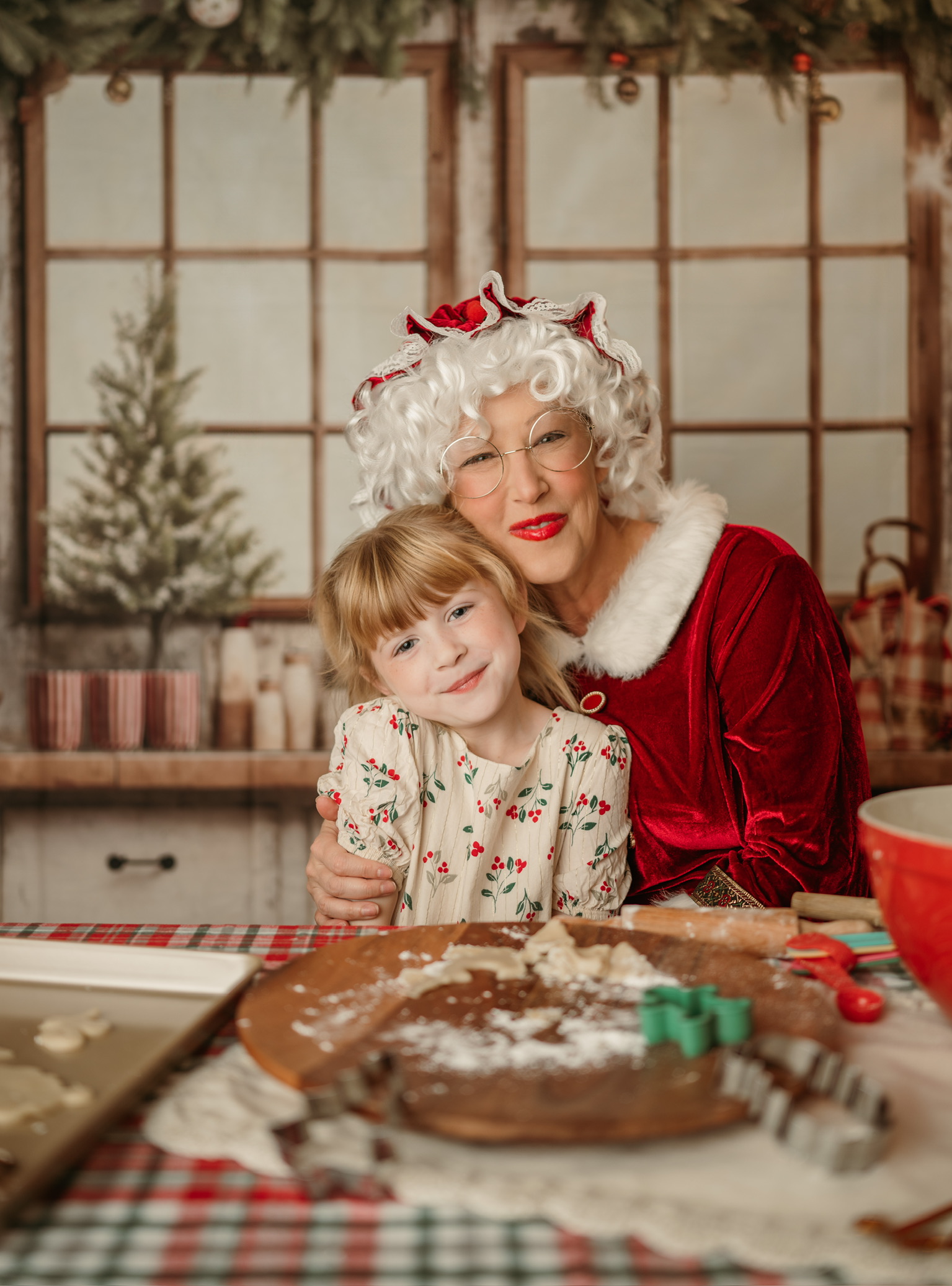 Mrs. Claus in her red velvet dress and round gold glasses sharing a sweet moment with a smiling little girl.
