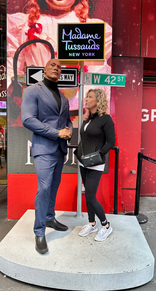 Mandy, The Empty Nest Mom, posing with a celebrity wax figure in a blue suit outside Madame Tussauds New York on West 42nd Street in Times Square